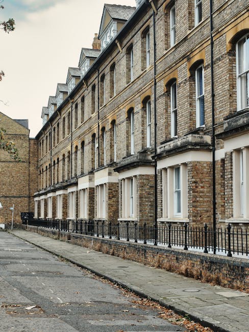 A row of elegant, white Victorian-style residential buildings with ornate architectural details, including decorative window moldings and black wrought iron balconies, situated along a street in Maida Vale. The facades are clean and well-maintained, with sunlight illuminating the intricate cornices and smooth surfaces. Lampposts line the sidewalk in front of the buildings, and leafless trees are visible in the foreground. The scene captures a tidy and picturesque residential area, highlighting the importance of surface cleaning and regular maintenance, as offered by Maida Vale Cleaners, in ensuring the aesthetic appeal and hygiene of properties in Sutherland Avenue.